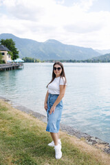 Beautiful female in denim skirt posing to photographer in front of big beautiful lake with clear water