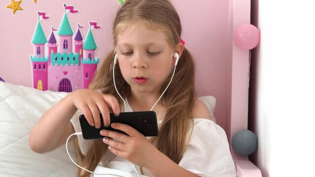 A young girl in headphones flips the phone screen horizontally, The child turned on the movie on the smartphone and looks. Dependence on the gadgets of modern mankind is a problem of the modern world.