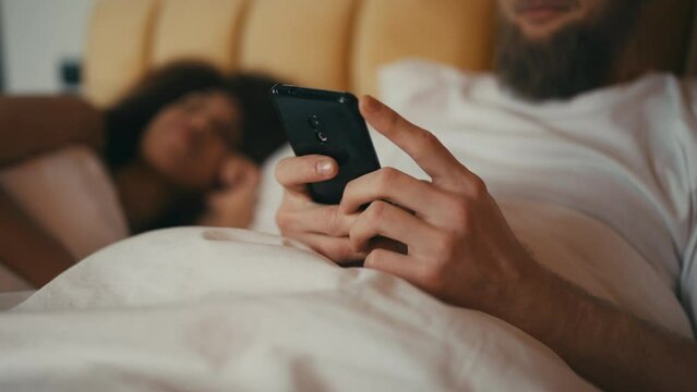 Closeup of man texting mistress while his wife is asleep, dating app user