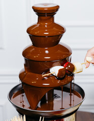 Chocolate fountain with marshmallows, strawberries and banana on a wooden skewer