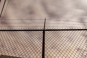 vue sur la silhouette d'une cl&ocirc;ture en m&eacute;tal avec trois rang&eacute;es de fil barbel&eacute; au dessus lors d'une nuit ennuag&eacute;e
