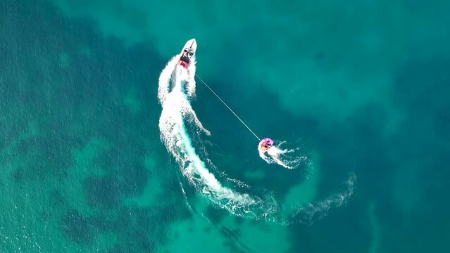 Tubing boat with people moving behind the boat on the water. Aerial view of motor speed boat pulls inflatable rubber raft with people. Summer vacation shot