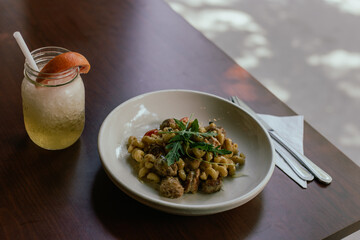 Bol de macaroni au fromage à la viande dans un bol blanc déposé sur une table en bois avec un cocktail en lumière naturelle