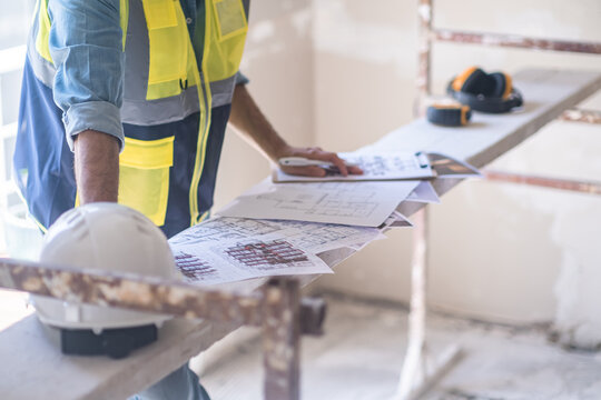 Worker checking renovation project papers put on construction equipment near helmet man in professional uniform doing paperwork before reconstruction process in apartment