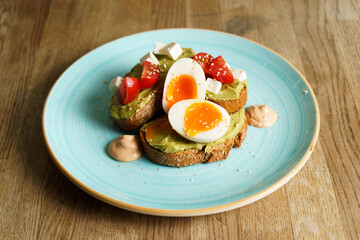 Avocado toast with guacamole, soft boiled egg, cream cheese and tomatoes on a plate