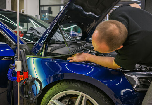 A specialist repairs a dent on the car body without painting. Process of paintless dent repair on car body. The mechanic at the auto shop with tools to repair dents in car body. Body repair. PDR. 
