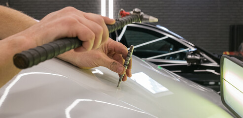 A specialist repairs a dent on the car body without painting. Process of paintless dent repair on car body. The mechanic at the auto shop with tools to repair dents in car body. Body repair. PDR. 