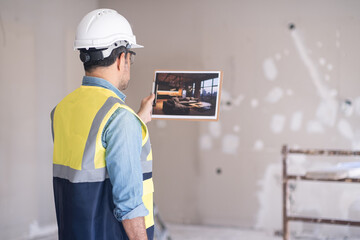 Experienced worker in protective helmet looking at picture of loft-style interior in hand...