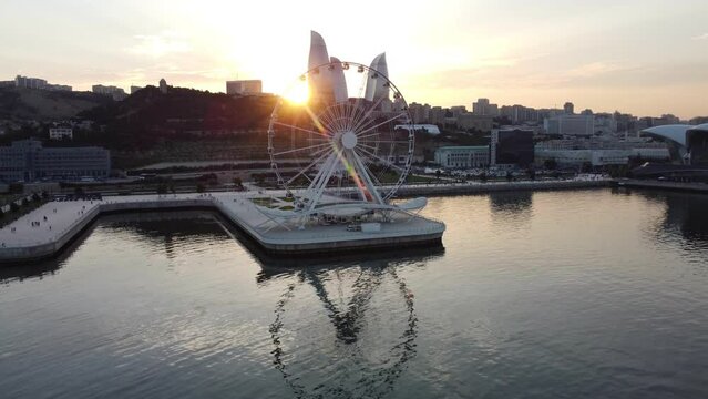 Baku, Azerbaijan - June 27, 2023: Aerial drone footage capturing a mesmerizing sunset behind the Flame Towers, approaching from the sea and over the Baku Eye Ferris wheel