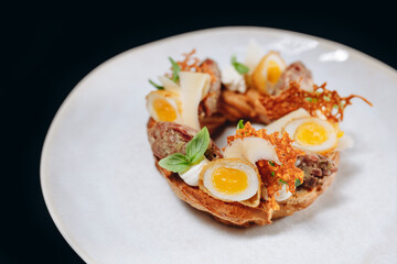 Bruschetta with meat and quail eggs on a white plate