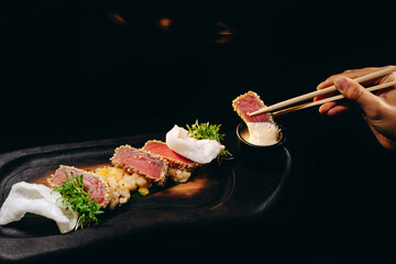 A piece of tuna in Chinese chopsticks in hand on the black background