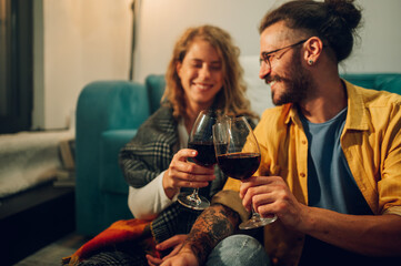 Focus on two glasses of red wine clinking with blurred background of a couple.