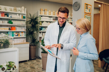 Portrait of a male pharmacist helping a senior woman patient in pharmacy