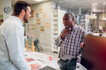 Senior african american man patient buying drugs from a male pharmacist in a drugstore