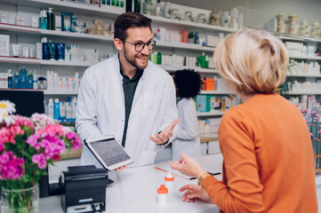 Portrait of a male pharmacist working at the counter in pharmacy - obrazy, fototapety, plakaty