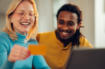 Fototapeta premium A cheerful interracial couple is sitting at home and shopping online with a credit card.