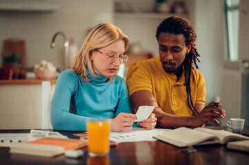 A serious multicultural couple is sitting at home and looking at high bills and taxes.