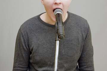 Young man's mouth wide open in front of a microphone. Loud shouting, public emotional reaction..