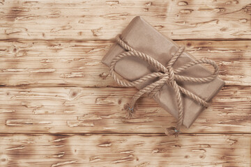 A rectangular box with a present wrapped in craft paper and tied with a linen rope lies on a wooden...