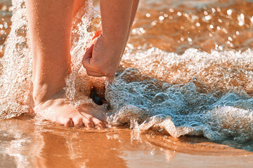 Child 10-11 years old plays on the beach in summer. A girl stands barefoot on the sand and is washed by the waves of the sea.