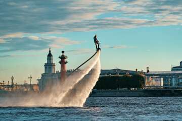 A man flies over water on a flyboard in the city river, rising into the air due to the water jet....