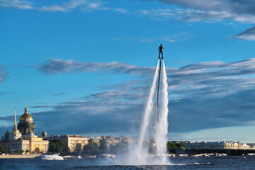 A man took off high above the water on a flyboard in the river of a beautiful city. A sportsman is...