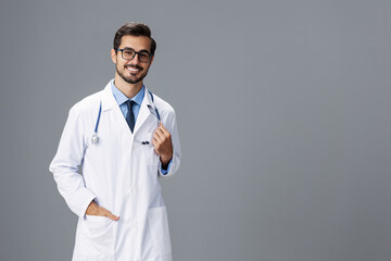 A serious doctor man in a white coat and eyeglasses and a stethoscope looks at the camera on a gray isolated background, copy space, space for text, health