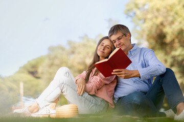 Romantic mature couple reading books while spending free time together outdoors