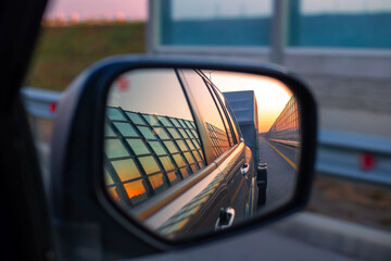 View in the mirror of the side view of the car on the road and caravan at dawn. Trucking and travel