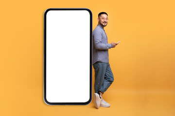 Smiling Asian Man Holding Smartphone And Leaning At Huge Blank Cellphone