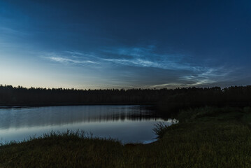 Noctilucent clouds over the forest lake in Latvia at July night
