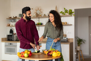 Cheerful young arab husband and wife enjoying cooking together, preparing healthy dinner and chatting, copy space