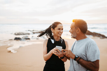 Cheerful senior caucasian lady and man in sportswear use phone app, enjoy training and active lifestyle on beach