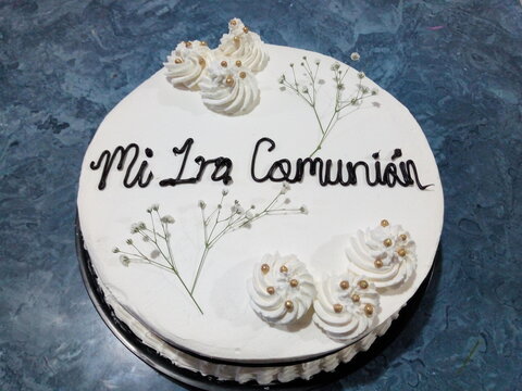 Pastel  blanco de primera comunion con flores, perlas y rosetones de decoracion sobre un fondo azul