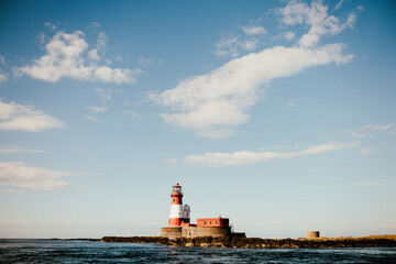 Obraz premium Red and White lighthouse on an island surrounded by sea and blue skies