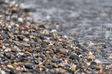 Close-up of pebble beach with light reflecting on colored stones against the waves in the background