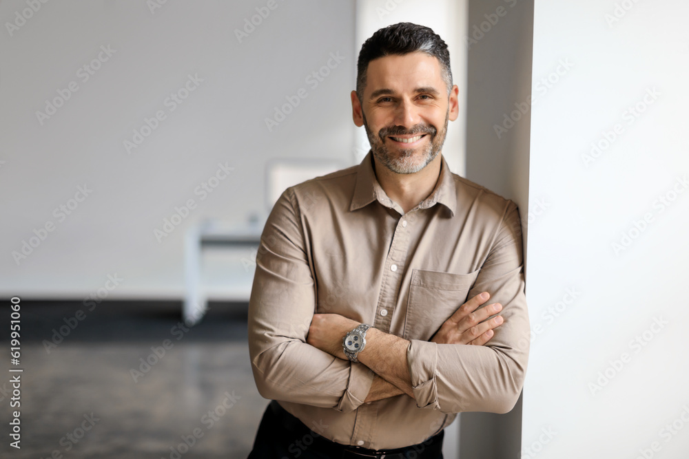 Canvas Prints smiling european middle aged businessman standing in office, posing with folded arms and leaning on 