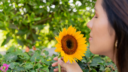 mujer joven, sonriendo y sosteniendo un girasol en un día soleado de primavera en un parque,...