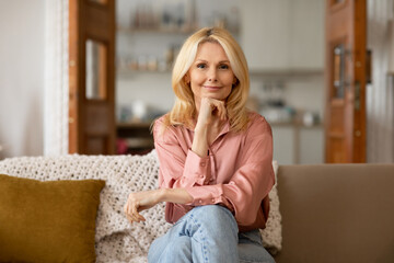 Happy Mature Blonde Woman Posing Sitting On Sofa At Home