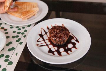 Chocolate pancake covered with chocolate frosting on top of a dark glass table.