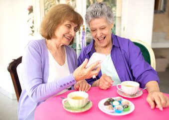 Obraz na płótnie Canvas Cheerful senior women using phone while having coffee at cafe
