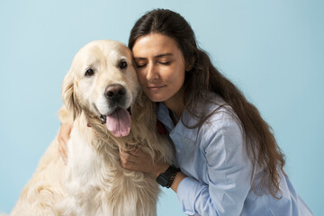 Cute woman with long hair with closed eyes huging dog, golden labrador, isolated on blue background