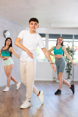 Fototapeta na wymiar Guy and young girls in good mood actively move and dance reggaeton at choreography lesson. Leisure activity, hobby