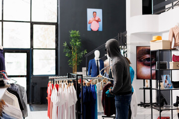 Robber wearing hood and sunglasses, trying to sneak stolen trendy merchandise from modern boutique....