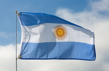 Large flag of Argentina fixed on metal stick waving against background of cloudy sky during daytime