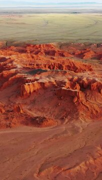 Aerial around view of the Bayanzag flaming cliffs at sunset in Mongolia, found in the Gobi Desert. Vertical video