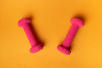 two pink dumbbells for fitness on yellow background