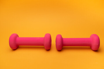 two pink dumbbells for fitness on yellow background