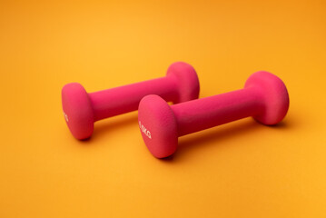 two pink dumbbells for fitness on yellow background