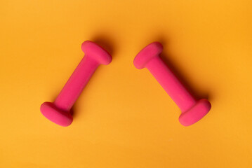 two pink dumbbells for fitness on yellow background